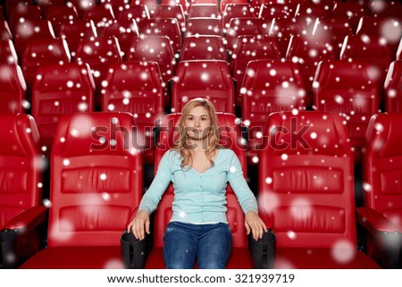 cinema, entertainment and people concept - young woman watching movie alone in empty theater auditorium with snowflakes
