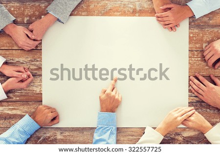 business, people and team work concept - close up of creative team sitting at table and pointing finger to blank paper in office