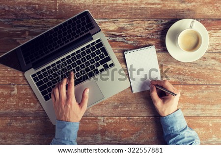 business, education, people and technology concept - close up of male hands with laptop and coffee cup taking notes to notebook by pen