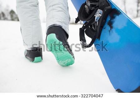 winter, leisure, sport and people concept - close up of snowboarder legs walking with snowboard outdoors