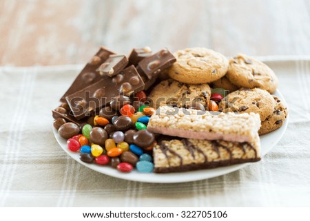 junk food, sweets and unhealthy eating concept - close up of chocolate, oatmeal cookies, candies and muesli bars on plate