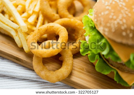 fast food, junk-food and unhealthy eating concept - close up of hamburger or cheeseburger, deep-fried squid rings and french fries on wooden table