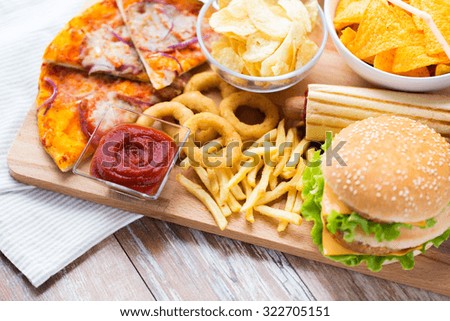 fast food and unhealthy eating concept - close up of hamburger or cheeseburger, deep-fried squid rings, french fries, pizza and ketchup on wooden table top view