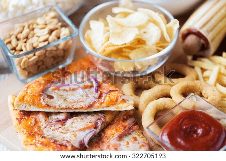 fast food and unhealthy eating concept - close up of pizza, deep-fried squid rings, potato chips, peanuts and ketchup on wooden table top view