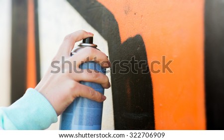 people, art, creativity and youth culture concept - close up of hand drawing graffiti with spray paint on street wall