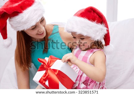 christmas, holidays, family, childhood and people concept - happy mother and little girl in santa hats with gift box at home