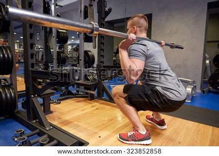 sport, fitness, bodybuilding, lifestyle and people concept - young man with bar of barbell flexing muscles in gym