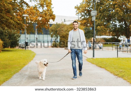 family, pet, domestic animal, season and people concept - happy man with labrador retriever dog walking in autumn city park