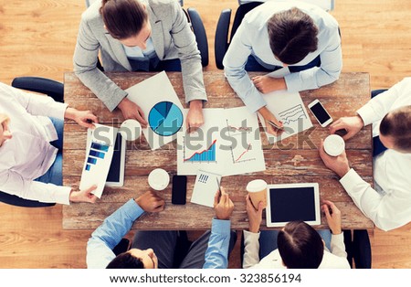business, people, statistics and team work concept - close up of creative team with charts and gadgets meeting and drinking coffee in office