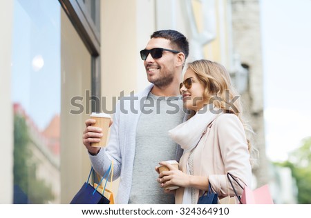 sale, consumerism and people concept - happy couple with shopping bags and coffee paper cups looking at shop window in city