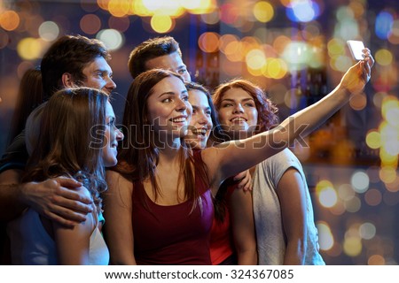 party, technology, nightlife and people concept - smiling friends with smartphone taking selfie in club