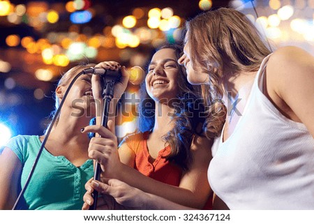 party, holidays, celebration, nightlife and people concept - happy young women singing karaoke in night club