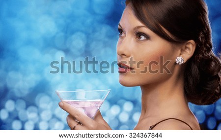 party, drinks, holidays, luxury and celebration concept - smiling woman in evening dress holding cocktail over blue lights background