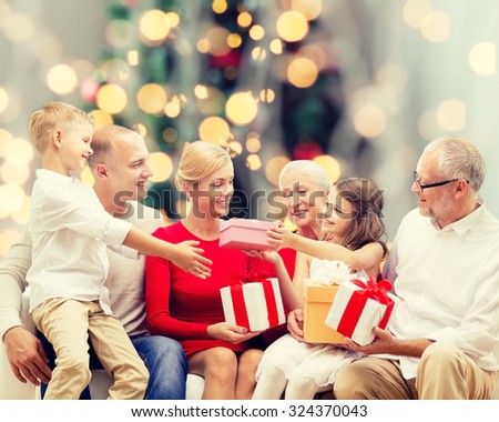 family, holidays, generation, christmas and people concept - smiling family with gift boxes sitting on couch over tree lights background