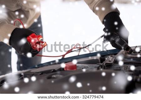 transportation, winter, people and vehicle concept - closeup of man under bonnet with starter cables