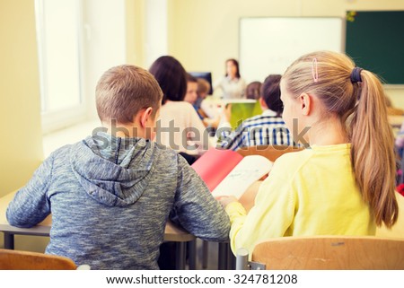 education, elementary school, learning and people concept - group of school kids with notebook writing test and helping in classroom
