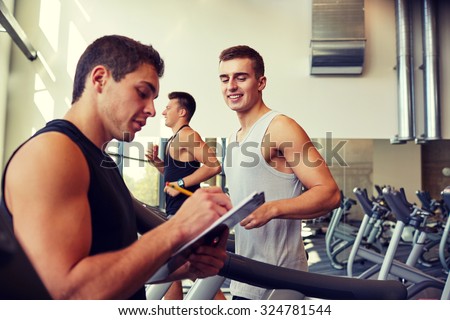 sport, fitness, lifestyle, technology and people concept - men with personal trainer exercising on treadmill in gym