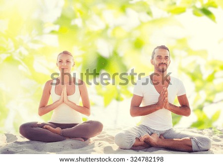fitness, sport, meditation and lifestyle concept - smiling couple making yoga exercises sitting outdoors