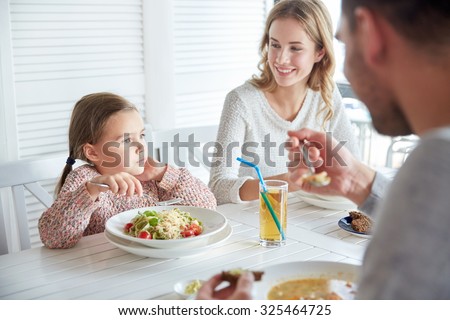 family, parenthood, food and people concept - happy mother, father and little girl eating pasta and soup for dinner at restaurant or cafe