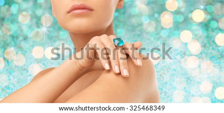 people, jewelry, luxury and glamour concept - close up of woman hand and ring with precious gem over blue lights background