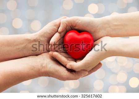 people, age, family, love and health care concept - close up of senior woman and young woman hands holding red heart over lights background