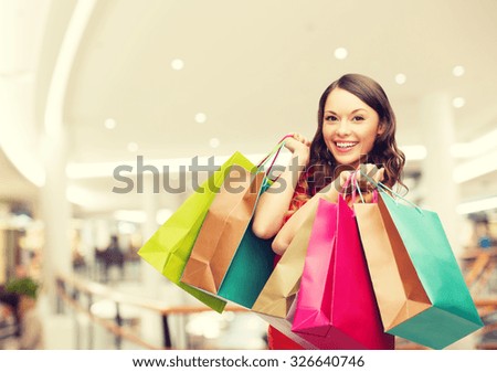 happiness, consumerism, sale and people concept - smiling young woman with shopping bags over mall background
