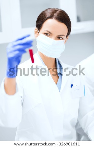 science, chemistry, biology, medicine and people concept - close up of young female scientist holding test tube with blood sample making research in clinical laboratory