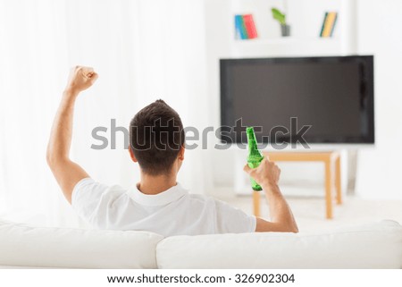 leisure, technology, mass media and people concept - man watching tv, supporting team and drinking bottle beer at home from back