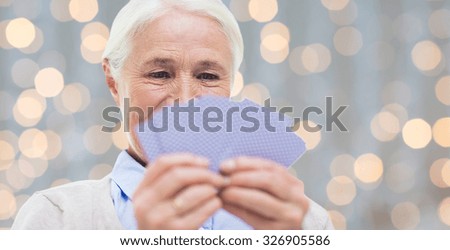 age, game, gamble, poker and people concept - close up of happy smiling senior woman playing cards over holidays lights background