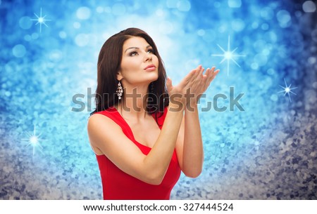people, holidays, christmas, magic and fashion concept - beautiful sexy woman in red dress blowing fairy dust off over blue glitter or lights background