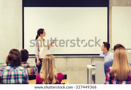 education, high school, technology and people concept - smiling student girl with remote control, laptop computer standing in front of white board and teacher in classroom