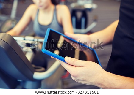 sport, fitness, lifestyle, technology and people concept - close up of trainer hands with tablet pc computer and woman working out on exercise bike in gym