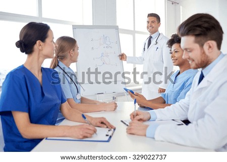 medical education, health care, medical education, people and medicine concept - group of happy doctors or interns with mentor meeting and drawing on flip board on presentation at hospital