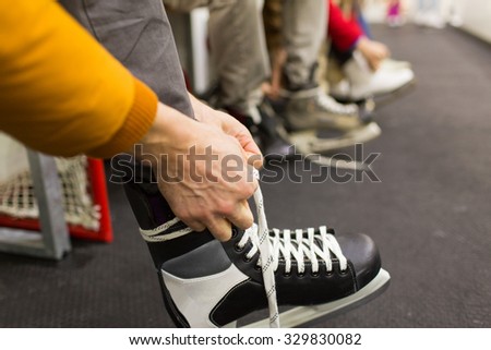 people, winter sport and leisure concept - close up of friends wearing and lacing skates on skating rink