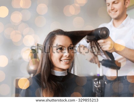 beauty, hairstyle and people concept - happy young woman and hairdresser with fan making hot styling at hair salon over holidays lights