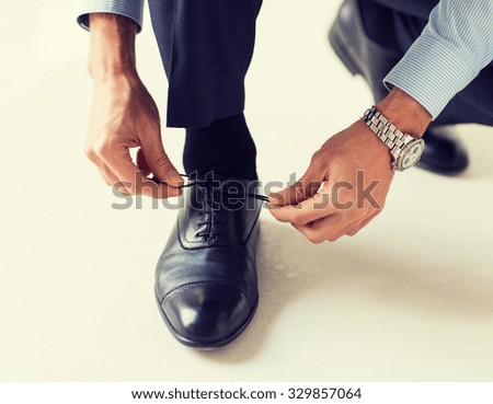 people, business, fashion and footwear concept - close up of man leg and hands tying shoe laces