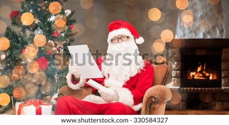 christmas, holidays, winter and people concept - man in costume of santa claus with letter sitting in armchair over home fireplace and lights background