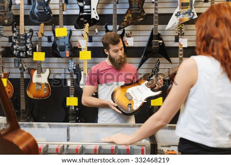music, sale, people, musical instruments and entertainment concept - assistant showing electric guitar to customer at music store