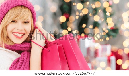 happiness, winter holidays and people concept - smiling young woman in hat and scarf with pink shopping bags over christmas tree background