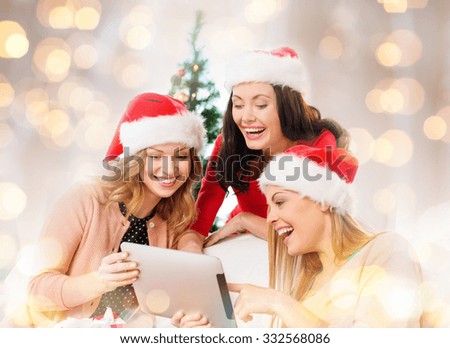 christmas, holidays, technology and people concept - happy women in santa helper hats with tablet pc computer over lights background