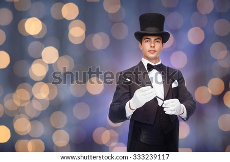 performance, circus, people and show concept - magician in top hat with magic wand over nigh lights background