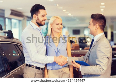 auto business, car sale, technology, gesture and people concept - happy couple with car dealer shaking hands in auto show or salon