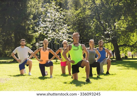 fitness, sport, friendship and healthy lifestyle concept - group of happy teenage friends or sportsmen exercising and stretching knee at boot camp