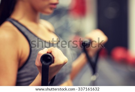 sport, fitness, lifestyle and people concept - close up of young woman flexing muscles on cable gym machine