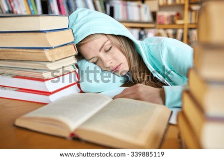 people, education, session, exams and school concept - tired student girl or young woman with books sleeping in library