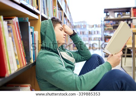 people, knowledge, education, literature and school concept - student boy or young man sitting on floor reading book in library