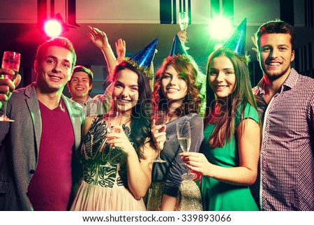 party, holidays, celebration, nightlife and people concept - smiling friends in party caps with glasses of champagne in club