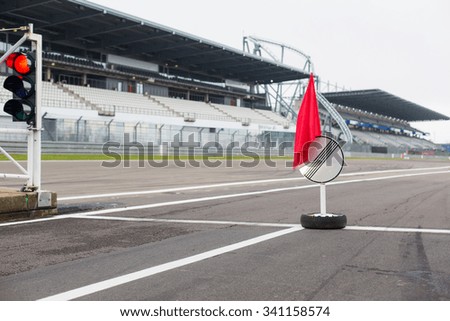 motosports, extreme and race concept - close up of red traffic lights and road sign with flag on speedway track or road