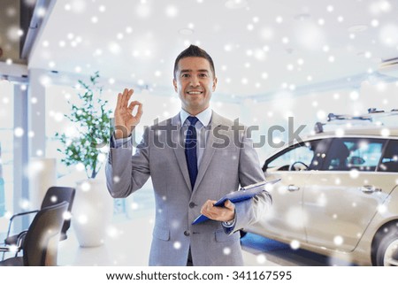auto business, car sale, consumerism, gesture and people concept - happy man with clipboard showing thumbs up at auto show or salon over snow effect