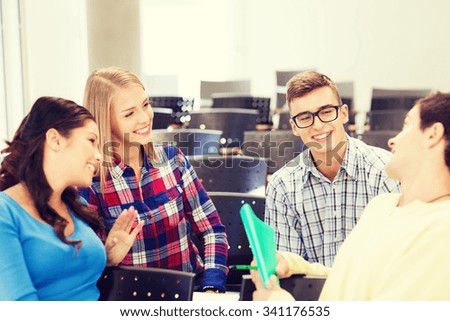 education, high school, teamwork and people concept - group of smiling students with notebook sitting in lecture hall and talking